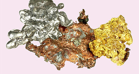three molten precious metals in misshapen lumps, silver, bronze and gold against a pink backdrop